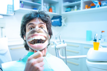 Giovane ragazzo seduto sulla poltrona del dentista, fa vedere il suo stupendo sorriso con la lente...