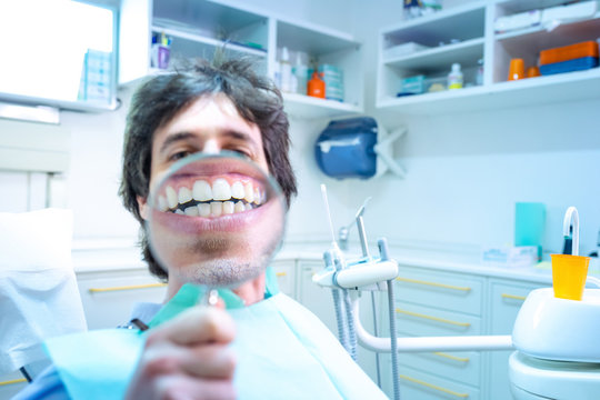 Giovane ragazzo seduto sulla poltrona del dentista, fa vedere il suo stupendo sorriso con la lente d'ingrandimento. Dopo aver fatto la pulizia dentale