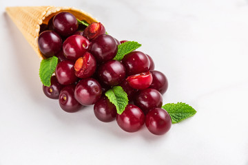 Summer cherry berries with mint in waffle cone on white marble background. summer food concept