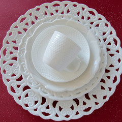 Top view of white vintage tableware set on red background. Empty elegant porcelain plates