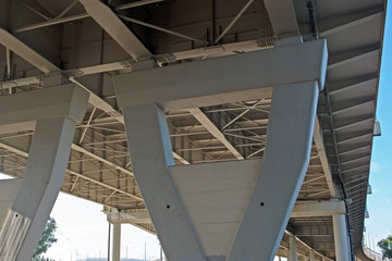 A long, white, curved trestle bridge stretching into perspective. Bottom view: supporting pillars of the structure, extending upwards and stiffeners under the bridge surface.