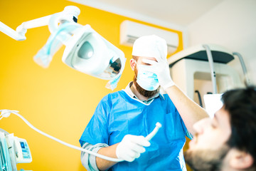 Obraz na płótnie Canvas Dentista odontoiatra incompetente si tocca il viso dopo aver fatto un pessimo lavoro sul suo paziente. Paura ad operare e delusione nel suo viso.