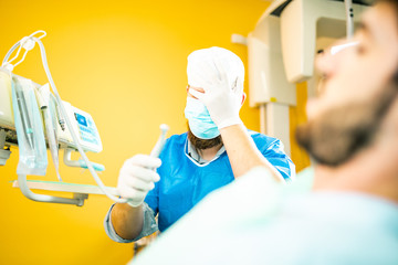 Fototapeta na wymiar Dentista odontoiatra incompetente si tocca il viso dopo aver fatto un pessimo lavoro sul suo paziente. Paura ad operare e delusione nel suo viso.