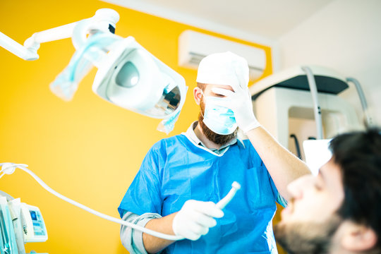 Dentista odontoiatra incompetente si tocca il viso dopo aver fatto un pessimo lavoro sul suo paziente. Paura ad operare e delusione nel suo viso.