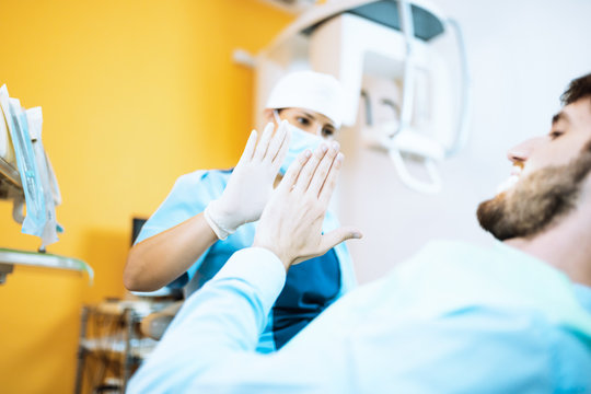 Giovane ragazza dentista odontoiatra da il cinque con la mano al paziente dopo l'operazione ai denti. Empatia con il paziente