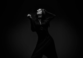 Black and white portrait of mysterious sensual beautiful brunette woman in black futuristic dress. High fashion model posing in studio on dark background.