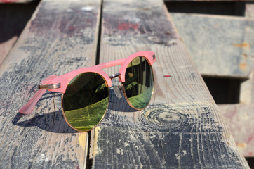 Pink sunglasses against the sun on a wooden background near the sea
