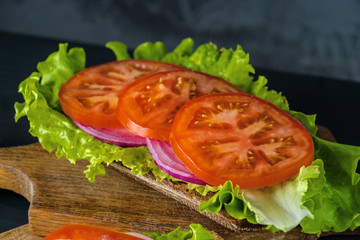 Breakfast tomato sandwich with salad on black wood background.