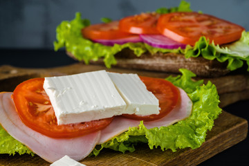 Breakfast tomato sandwich with salad on black wood background.