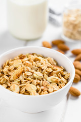 Homemade baked crunchy oatmeal, sliced almond, honey and coconut oil breakfast granola in bowl, ingredients and milk in the back (Selective Focus, Focus in the middle of the granola)