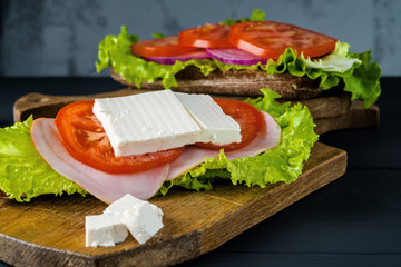 Breakfast tomato sandwich with salad on black wood background.