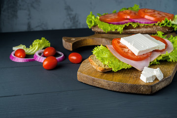 Breakfast tomato sandwich with salad on black wood background.