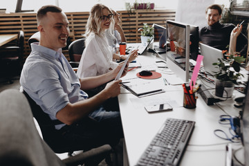 Young team of the colleagues works sitting at the desks with a laptop and documents in a light modern office