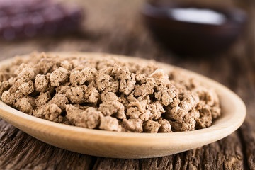 Raw dehydrated soy meat, soy protein, soya chunks or textured vegetable protein on wooden plate, photographed on rustic wood (Selective Focus, Focus in the middle of the image)