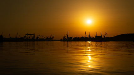 Beautiful sunset in the sea port. Orange sky with magically reflecting sun on the waves of the sea, Gdynia, Poland.