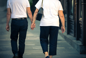 An older woman and a man walk around the city in the summer and hold hands