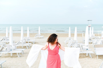 Obraz premium A woman in a red dress and curly hair is standing on the beach. A man with happy emotions. Walk along the sea promenade. Travel and tourism in the summer. Copy space
