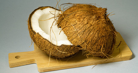 Coconut, exotic fruit, two halves of the fruit in the shell on a wooden board, light background, selective focus, close-up