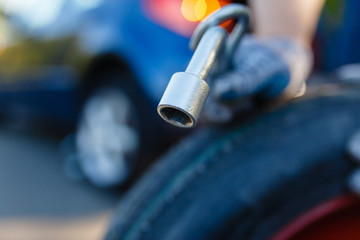 Close-up of a man's hand with spare wheel and cylinder key on the background of the car on the Jack. Mechanic wearing gloves with a spare wheel of a car with a flat wheel. Replacing tires on the road