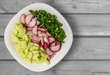 background of cucumbers, radish, and green onions. sliced for salad vegetables on a white plate on a wooden table, copy space