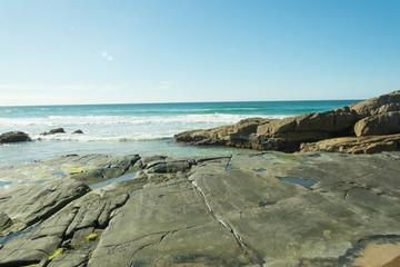 Fototapeta na wymiar Vista para a praia com um caminho de rocha que aparece na maré baixa.