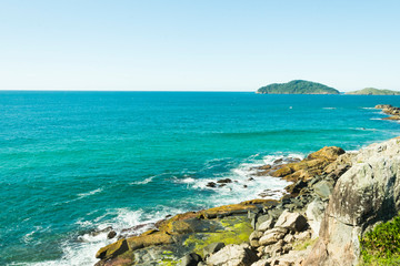 Fototapeta na wymiar Vista do alto de um rochedo para o mar e uma ilha deserta florestada ao horizonte.