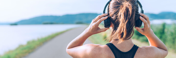 Young teenager girl adjusting  wireless headphones before starting jogging and listening to music. Web page header cropping.