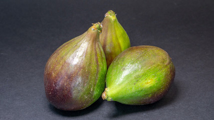 Green figs, three fruits on a light dark background, close-up