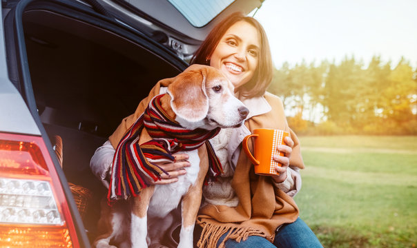 Woman with dog sit together in cat truck and warms цшер hot tea. Auto travel with pets concept image.