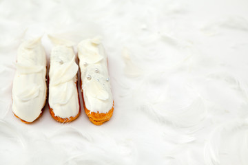 A set of three eclairs with white chocolate decor isolate on a white surface decorated with white feathers