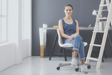 Young woman sitting at the desk with instruments, plan and laptop.