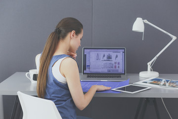 Young woman sitting at the desk with instruments, plan and laptop.