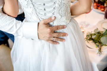 The groom hugs the bride. The hand of the groom on the back of the bride.