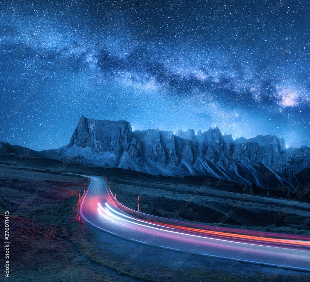 Wall mural milky way over mountain road at night in summer. blurred car headlights on winding road. colorful la