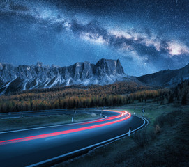 Milky Way over mountain road at night. Blurred car headlights on winding road in autumn. Beautiful...