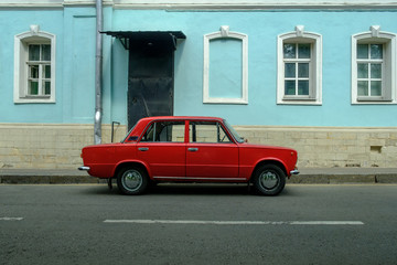 red retro car near blue retro building on street