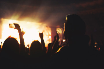 Silhouette of a concert crowd. The audience applauds the musicians on stage. The bright spotlight and dancing people.