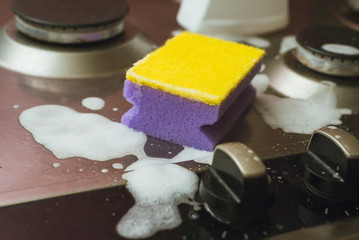 Violet - yellow sponge with a metal gas stove. Cleaning the dirt with a sponge with foam.