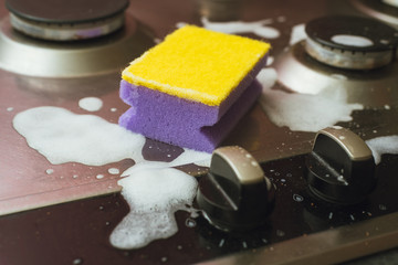 Violet - yellow sponge with a metal gas stove. Cleaning the dirt with a sponge with foam.