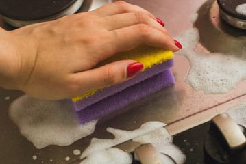 Violet - yellow sponge with a metal gas stove. Cleaning the dirt with a sponge with foam.