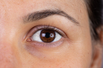 A macro view on the eye of a beautiful young woman with brown iris. Slight redness can be seen in...