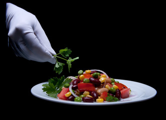 Healthy bean and corn salad on a white plate served by someone in white gloves