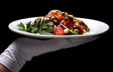 Healthy bean and corn salad on a white plate served by someone in white gloves
