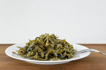 Pickled kelp slices and a fork on a plate over brown wooden table. Edible seaweed contains a lot of iodine and microelements. Seafood, vegetarian nutrition and healthy eating.
