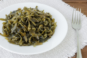 Plate with slices of pickled kelp and a fork on a fringed table napkin. Edible seaweed contains a lot of iodine and microelements. Seafood, vegetarian nutrition and healthy eating.