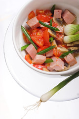 Delicious salad of ham, tomato, pepper and green onion on a white plate.