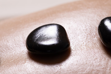 A close up view of a hot stone on the back of a naked woman at a spa. Alternative medicine therapy to help rest and relax the spinal muscles.