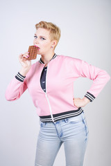 pretty plus size adult girl with short hair love chocolate. cheerful young woman enjoys sweet food. cute curvy lady in pink sport jacket holds chocolate bar in her hands on white studio background.