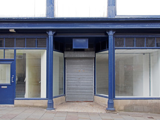 the facade of an old abandoned shop painted blue and white with empty store front dirty windows and closed shutters on the door