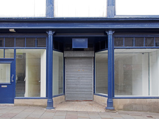 the facade of an old abandoned shop painted blue and white with empty store front dirty windows and...
